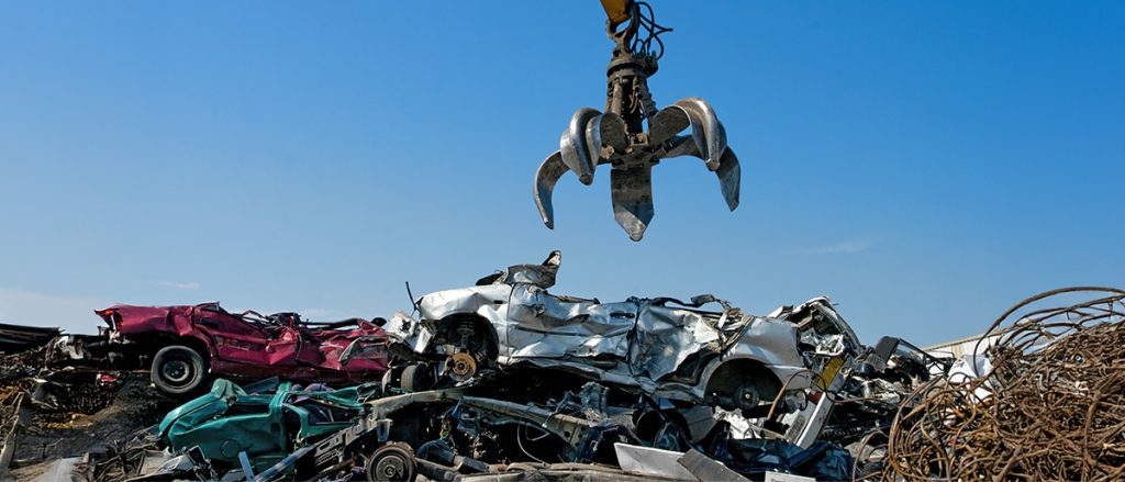 Claw grabbing a scrapped car off a metal pile